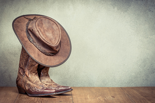 Viejo frente de botas y sombrero de vaquero de cuero retro salvaje oeste fondo de pared de hormigón. Foto filtrada de estilo vintage de instagram photo