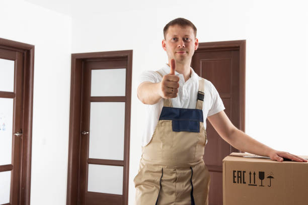Mover holds thumb up. Relocation services man. Loader in house with cardboard boxes stock photo