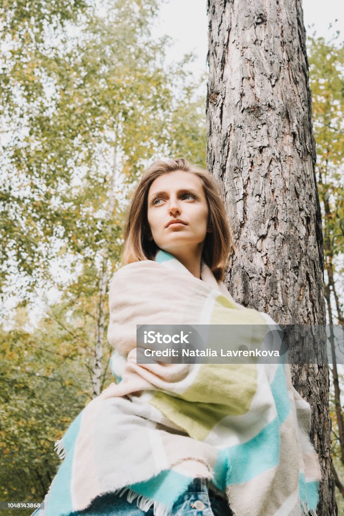 Lifestyle portrait of young adult female wrapped in her scarf in the forest or park Adult Stock Photo