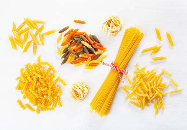istock assorted raw pasta flat lay on white. spaghetti fusilli penne tagliatelle girandole 1048148910