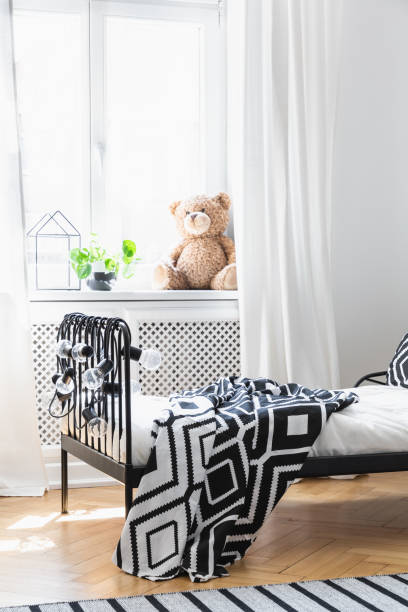 istock Patterned black and white blanket on bed in bedroom interior with plush toy on window sill. Real photo 1048150156