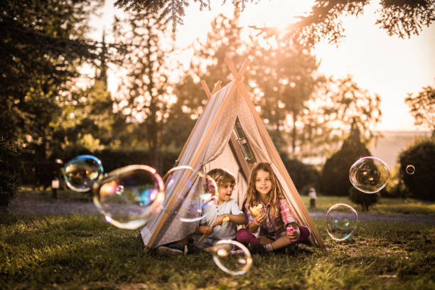 niños pequeños jugando con la varita de la burbuja frente a una tienda de campaña al aire libre. - bubble wand bubble child playful fotografías e imágenes de stock