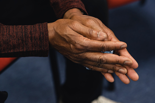Close up shot of a mature man's hands while he is sitting in a support group circle, holding a tissue.