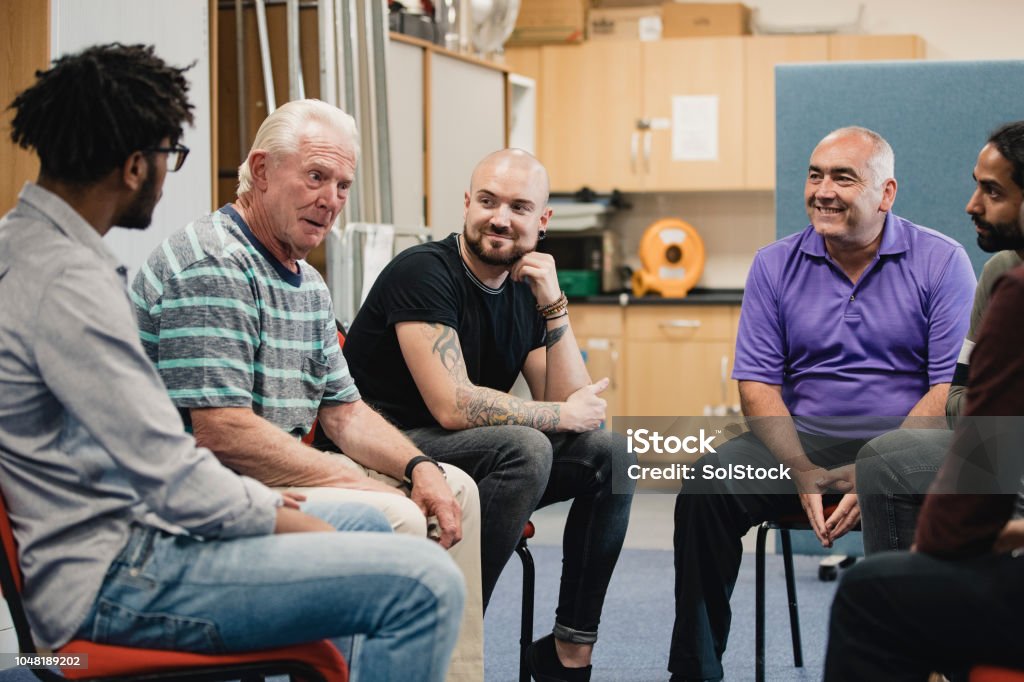 Men in a Support Group Diverse group of men are talking and laughing together in a mental health support group. Men Stock Photo