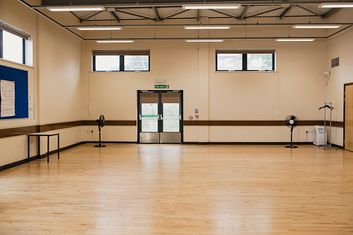 Empty school gymnasium with a fire exit and electric fans.