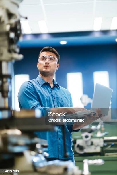 Latin Engineer Working On Laptop And Drill Stock Photo - Download Image Now - Engineer, Technology, Industry
