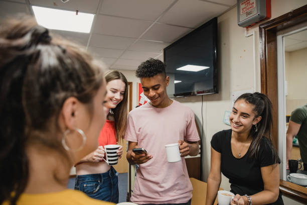 Teenagers Relaxing at Youth Club Small group of teenagers are talking and enjoying cups of tea at youth club. The boy is using his smart phone. teenagers only teenager multi ethnic group student stock pictures, royalty-free photos & images
