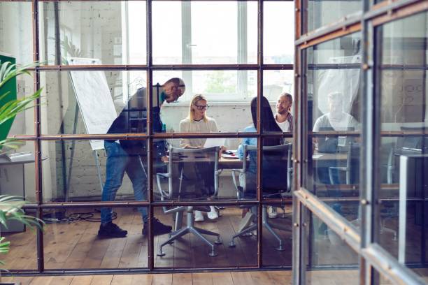 young professional team. group of young modern people in smart casual wear having a brainstorm meeting while standing behind the glass wall in the creative office. - estúdio de design imagens e fotografias de stock