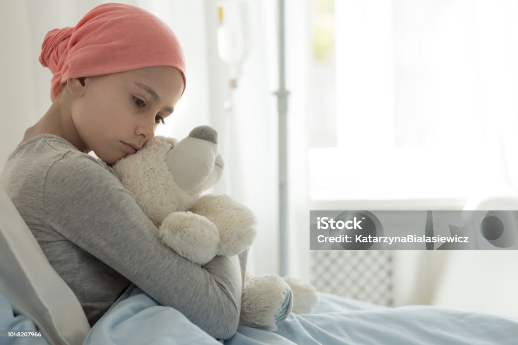 Weak girl with cancer wearing pink headscarf and hugging teddy bear Child Stock Photo