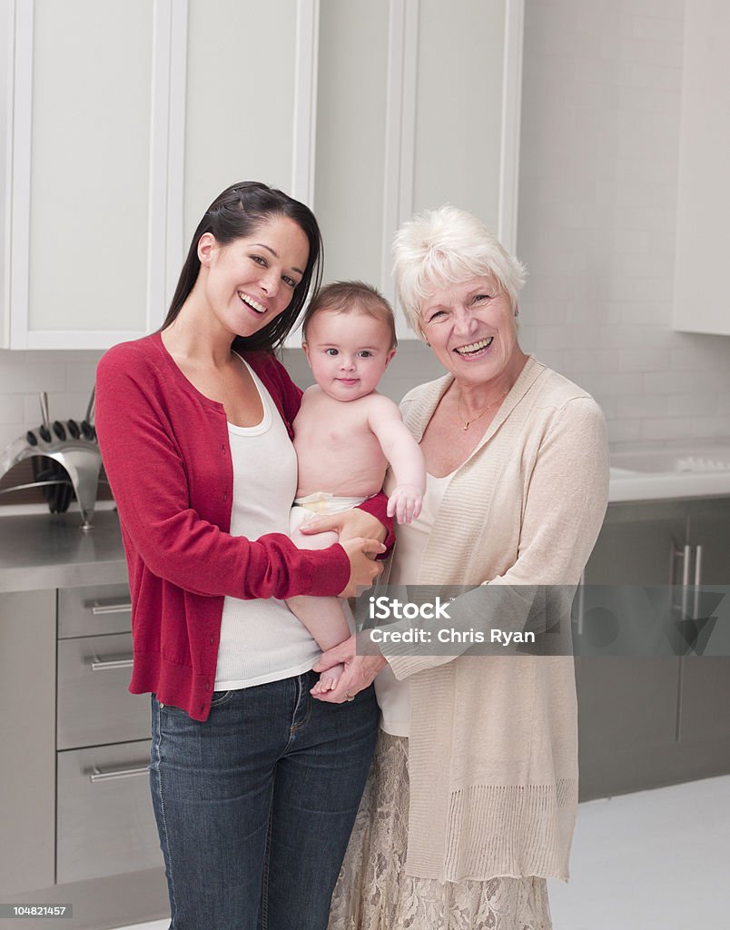 Улыбающаяся бабушка и мать держит ребенка в kitchen - Стоковые фото Младенец роялти-фри