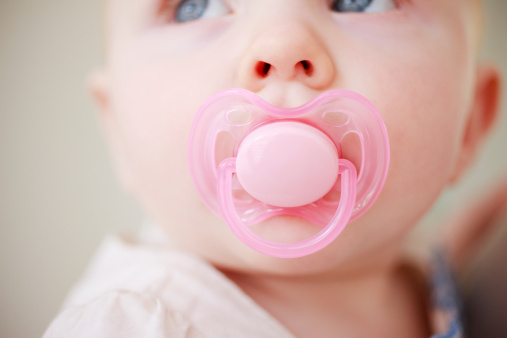 Extreme close up of happy little baby with big eyes looking up with a pacifier and a blue hat outdoor