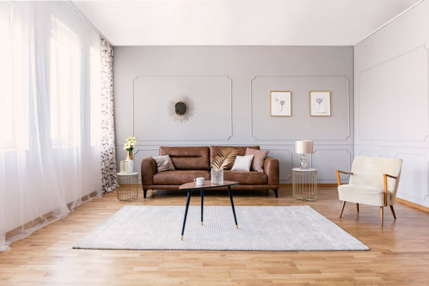 brown leather sofa in elegant living room interior with stylish armchair, coffee table and drawings on the grey wall - armchair sofa leather brown imagens e fotografias de stock