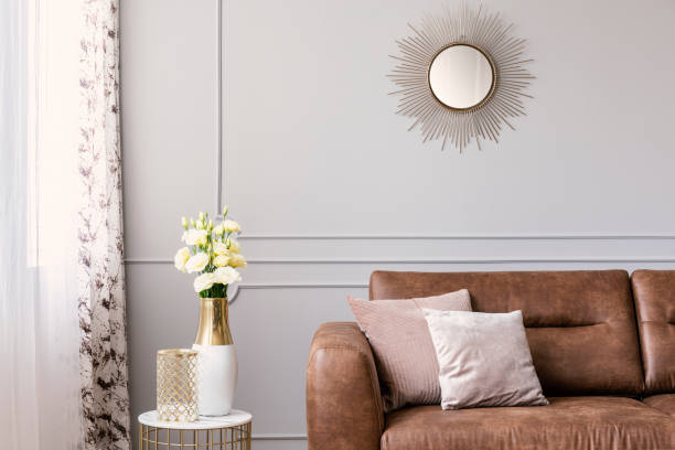 Sun like shaped mirror above leather sofa with pillows in grey elegant living room interior