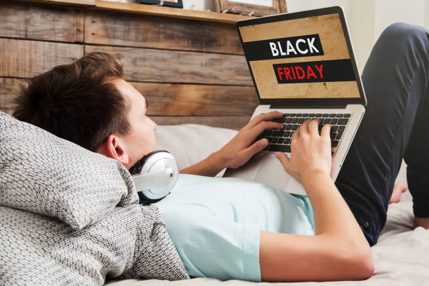 istock Man shopping on Black Friday special by the internet with a laptop computer, while lying down on the bed at home. 1048216554