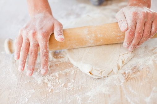 Working with handmade pasta. Close-up on a type of handmade pasta called fettuccine, left to rest on a wooden cutting board. Some useful tools for working: a rolling pin, a pastry wheel cutter and some flour to add to keep the consistency of the finished product soft.