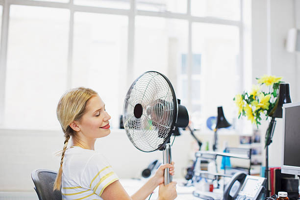 Smiling woman sitting in front of fan in office  electric fan photos stock pictures, royalty-free photos & images