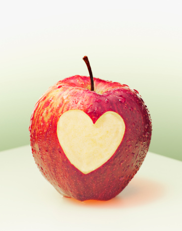 Green apple with heart shape half eaten in the center reflected on white table and white isolated background. Good health, nutrition and wellness concept. Front view.