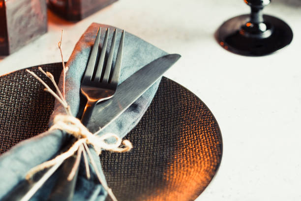 istock Festive table setting in a black style among black candles on a white table. Plate with fork and knife on a linen napkin. Thanksgiving or Halloween dinner. 1048228224