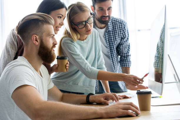 istock Discussing successful project. Group of young cheerful business people working and communicating while sitting at the office desk together with colleagues sitting in the background. 1048233434