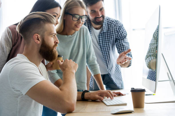 istock Discussing successful project. Group of young cheerful business people working and communicating while sitting at the office desk together with colleagues sitting in the background. 1048233436