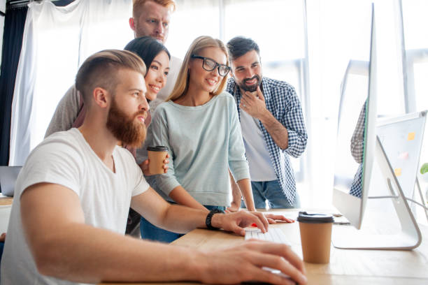 istock Discussing successful project. Group of young cheerful business people working and communicating while sitting at the office desk together with colleagues sitting in the background. 1048233588