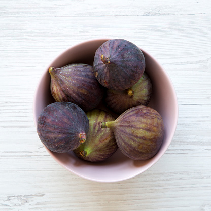 Fresh figs in a pink bowl on a white wooden background. Top view, overhead, from above.