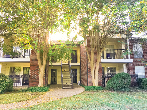 2-story apartment complex building in suburban North Texas, America in fall season sunset. Grassy lawn patio yard and autumn yellow dry leaves falling on the pathway near metal staircase