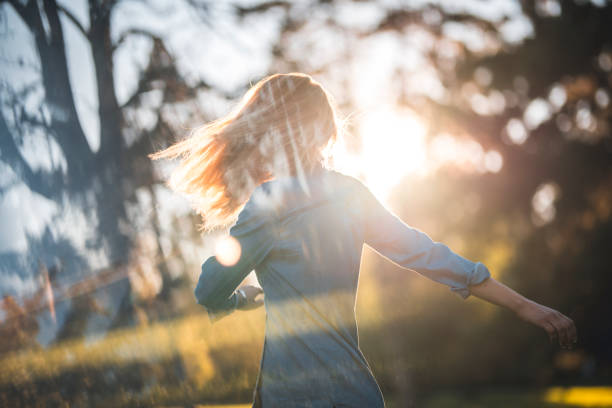 Woman enjoying in a park on a sunny summer day. She is spinning around and having fun. Sun is shining from back.