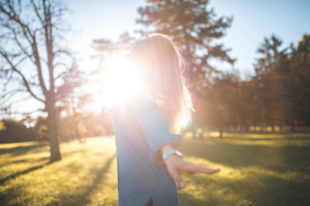 Woman enjoying in a park on a sunny summer day. She is spinning around and having fun. Sun is shining from back.