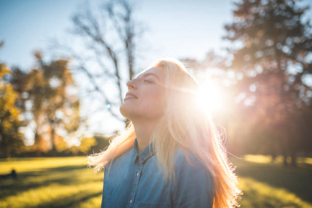 Woman enjoying in a park on a sunny summer day. She have her eyes closed, she is smiling and enjoying fresh air and sun.