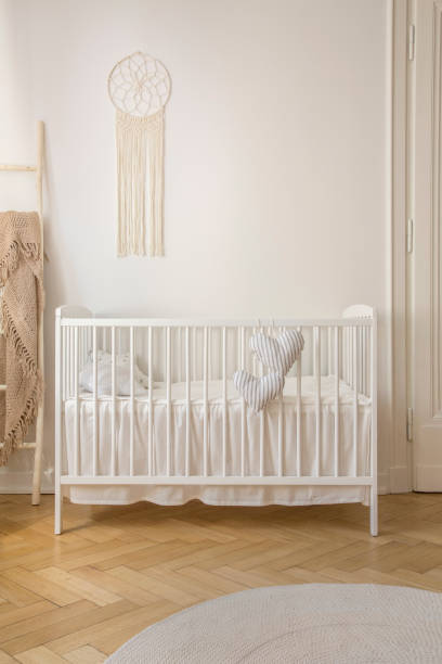 istock Two heart shaped pillows placed on baby crib standing in white room interior with macrame on wall and herringbone parquet in the real photo 1048248062