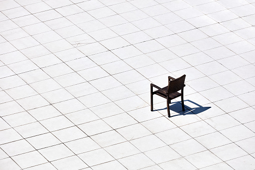 A minimalist view of a single chair and its shadow under the harsh sun on patterned white tile floors