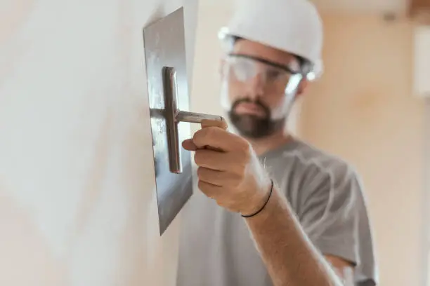Professional craftsman applying plaster with a trowel, home renovation concept