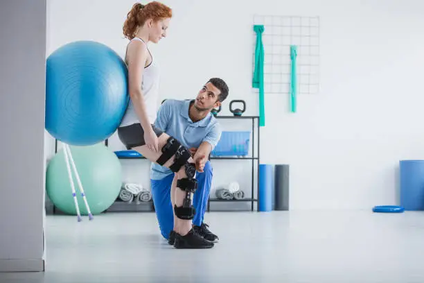 Photo of Woman with orthopedic problem exercising with ball while physiotherapist supporting her