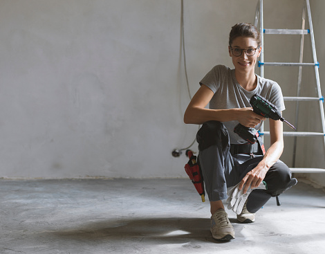 Professional repairwoman with tool belt doing a home renovation, she is posing and holding a drill