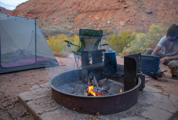 un pot de café cow-boy infuse sur le feu de bois tandis que le jeune homme branché prépare le petit déjeuner dans un camping à moab, utah. - coffee pot coffee break coffee cowboy coffee photos et images de collection