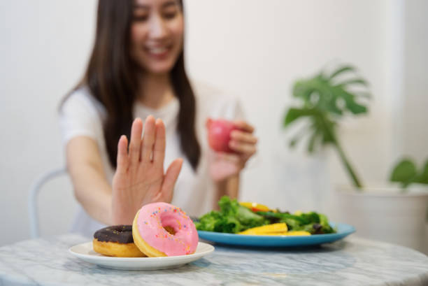 jeune fille sur un régime pour la notion de bonne santé. fermer vers le haut à l’aide de la main de femmes rejettent malbouffe en poussant sur ses beignets préférés et choisissez pomme rouge et salade pour une bonne santé. - entremets photos et images de collection