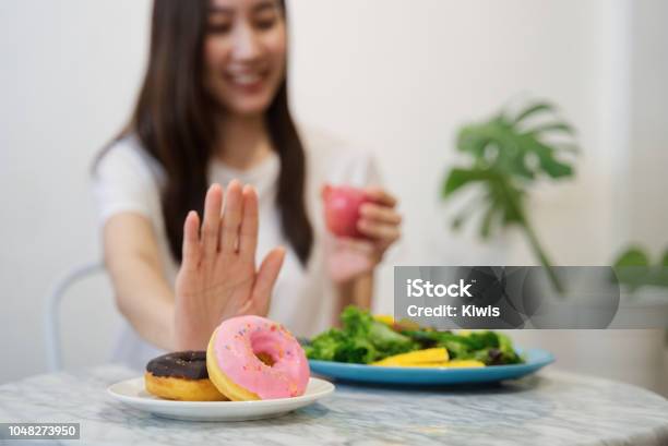 Young Girl On Dieting For Good Health Concept Close Up Female Using Hand Reject Junk Food By Pushing Out Her Favorite Donuts And Choose Red Apple And Salad For Good Health Stock Photo - Download Image Now
