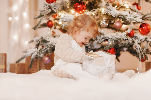 Family on Christmas morning. Baby girl opening Xmas presents. Children under Christmas tree with gift boxes. Decorated living room with christmas toys. Cozy warm winter day at white home.