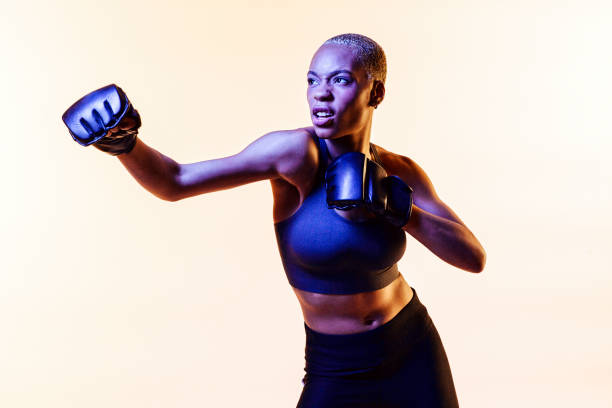 Fierce woman boxing, one arm stretched out Fierce woman boxing, one arm stretched out, isolated on a beige studio background boxing sport photos stock pictures, royalty-free photos & images