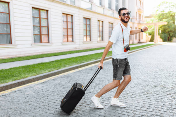 istock Positive traveler with a beard, with a suitcase and a camera, running through the streets, towards rest 1048285718