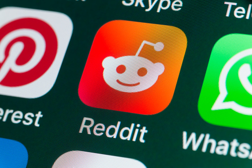 London, UK - July 31, 2018: The buttons of the app Reddit, surrounded by Pinterest, Whatsapp, and other apps on the screen of an iPhone.