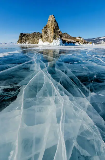 View of beautiful drawings on ice from cracks and bubbles of deep gas on surface of Baikal lake in winter with mountain, Russia