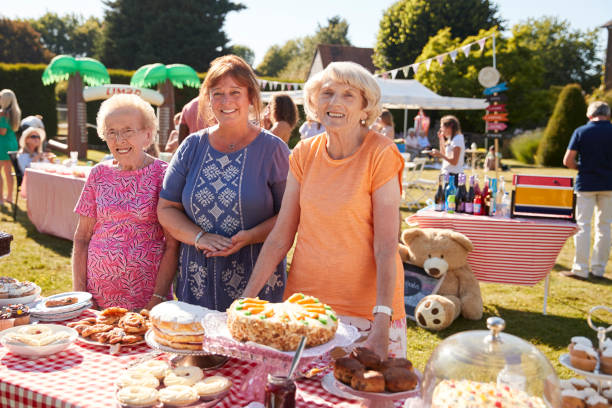 ritratto di donne che servono su una bancarella di torte nell'affollata festa del giardino estivo - fete foto e immagini stock