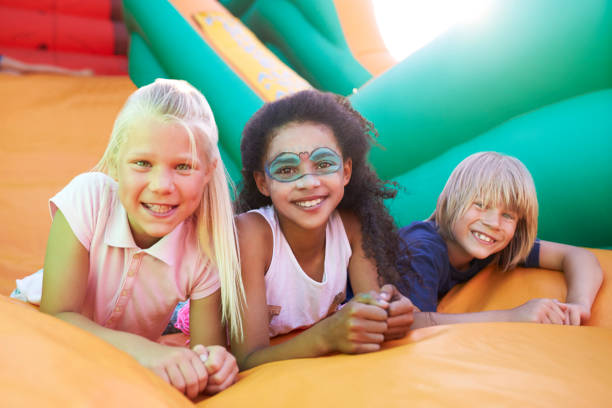 Portrait Of Children On Inflatable Slide At Summer Garden Fete Portrait Of Children On Inflatable Slide At Summer Garden Fete carnival children stock pictures, royalty-free photos & images