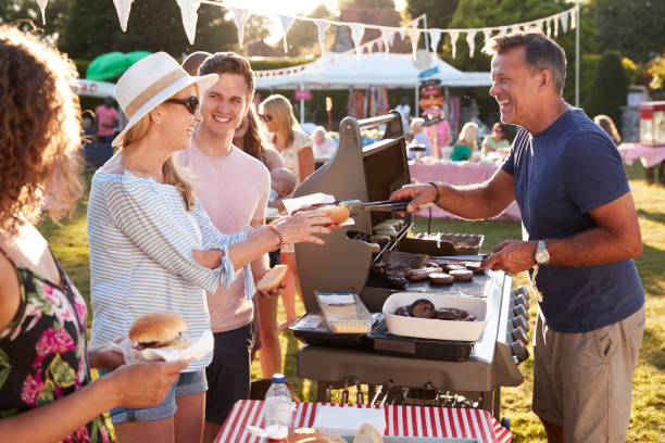 Man Serving On Barbeque Stall At Summer Garden Fete Man Serving On Barbeque Stall At Summer Garden Fete garden parties stock pictures, royalty-free photos & images