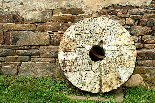 Old millstone leaning on a wall stock photo