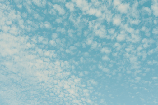 Pattern of white cirrus clouds on the pastel colored blue sky background.