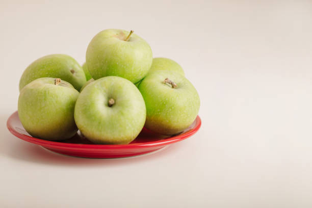 Red and green apples on a plate on a white background. Selective focus.