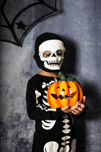 istock Young boy in the Skeleton costume holding Halloween pumpkin 1048372136